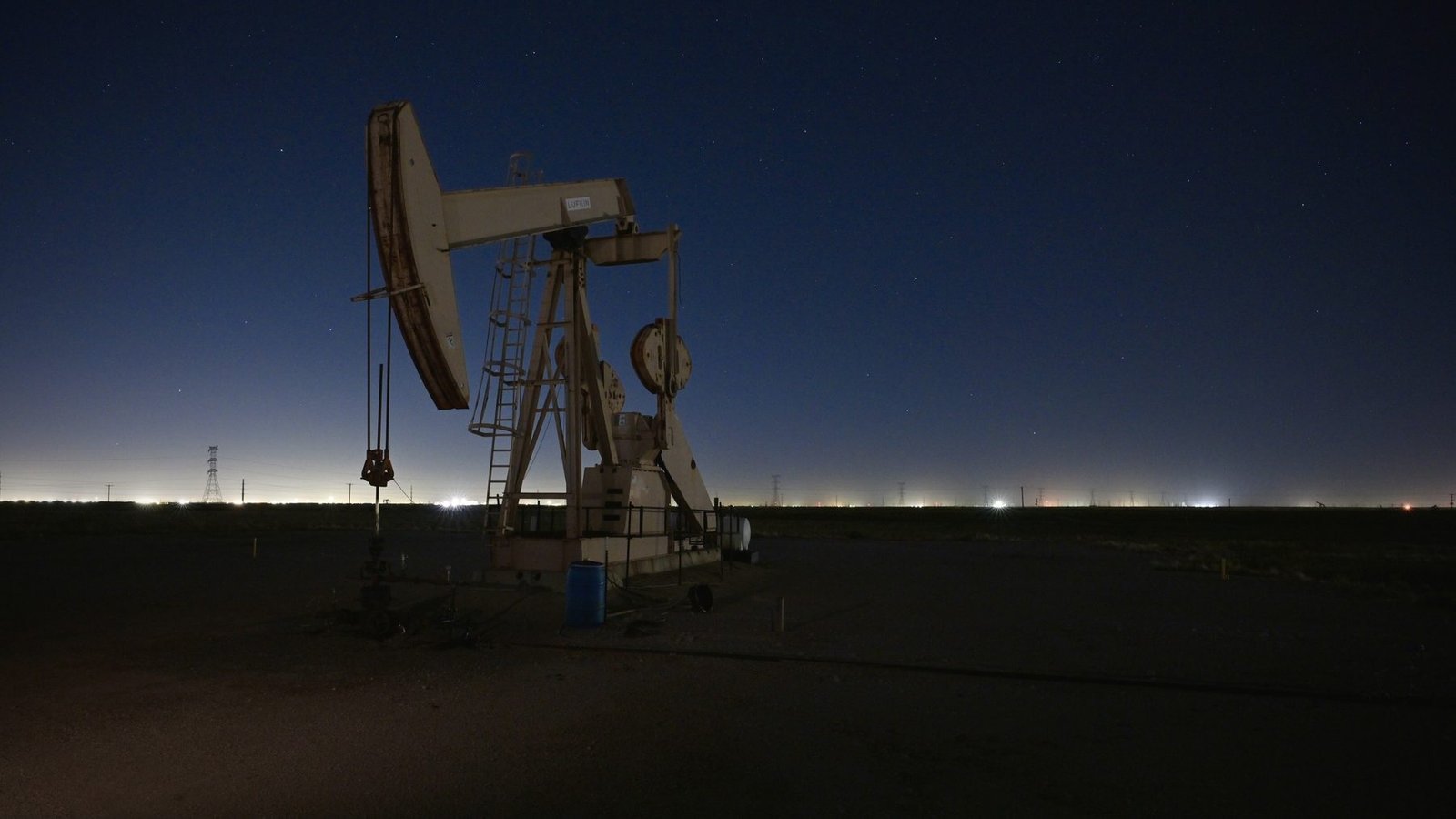 A pumping unit lit against a dark blue night sky with lights along the horizon