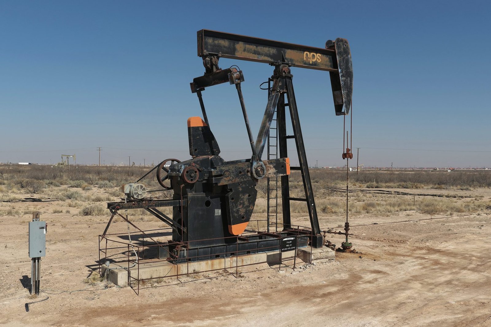 A black pumping unit on a bare dirt pad with an electrical box beside it